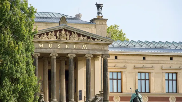 Historisches Museumsgebäude mit einer Skulptur im Vordergrund an einem sonnigen Tag.