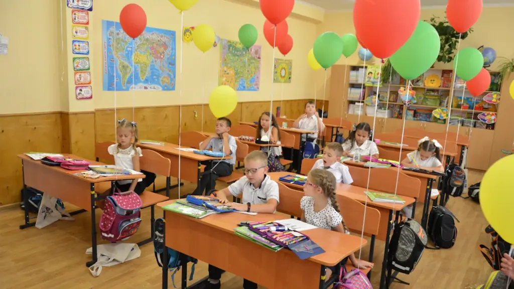 Grundschüler sitzen in einem mit Luftballons geschmückten Klassenzimmer an ihren Schulbänken.