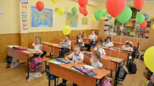 Grundschüler sitzen in einem mit Luftballons geschmückten Klassenzimmer an ihren Schulbänken.