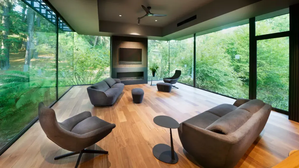 Modernes Wohnzimmer mit bodentiefen Fenstern und Blick in einen grünen Wald.