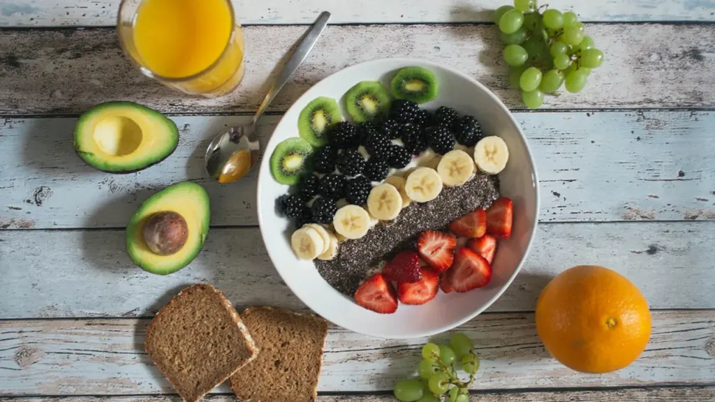 Gesundes Frühstück mit Avocado, frischen Beeren und Vollkornbrot auf einem rustikalen Holztisch.