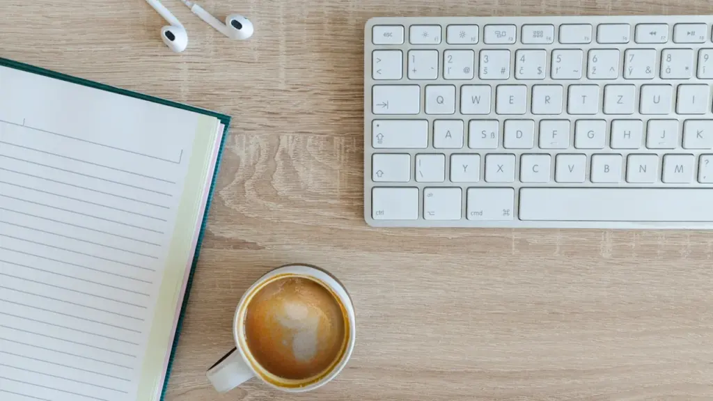 Ein sauberer Schreibtisch mit Laptop, Notizbuch, Kaffee und Kopfhörern für strukturierte Arbeitsplanung.