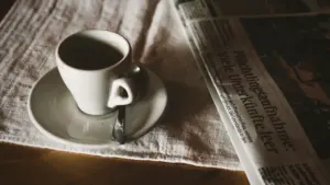 Tasse Kaffee und eine Zeitung mit Schlagzeilen auf einem Holztisch am Morgen.