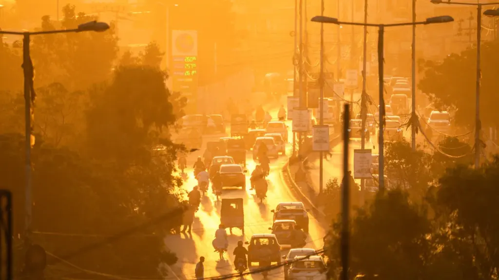 Dichte Stadtstraße mit Autos und Motorrädern in goldenem, staubigem Sonnenlicht bei Sonnenuntergang.