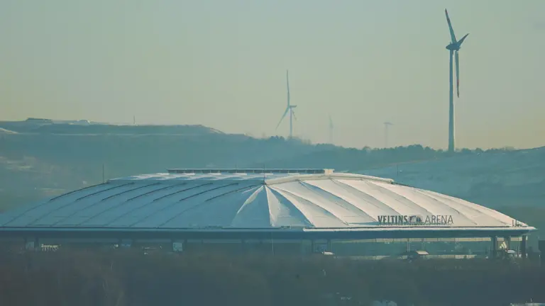 Die Veltins-Arena in Gelsenkirchen vor einer Kulisse mit Windkraftanlagen im Hintergrund.