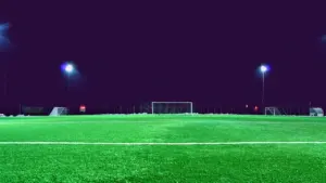 Ein beleuchteter Fußballplatz in der Dämmerung unter strahlendem Flutlicht am Abend.