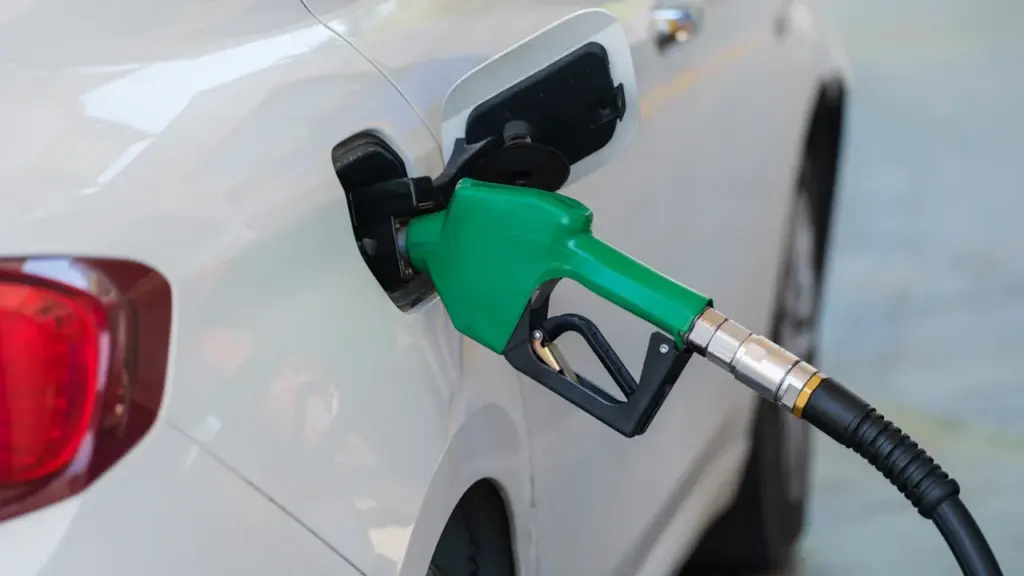 Eine grüne Zapfpistole beim Tanken eines weißen Autos an der Tankstelle.
