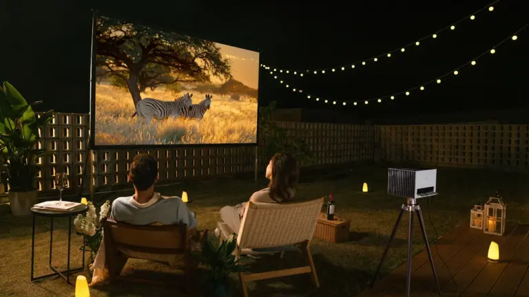 Ein Paar genießt abends entspannt einen Film im privaten Garten mit Lichterketten.
