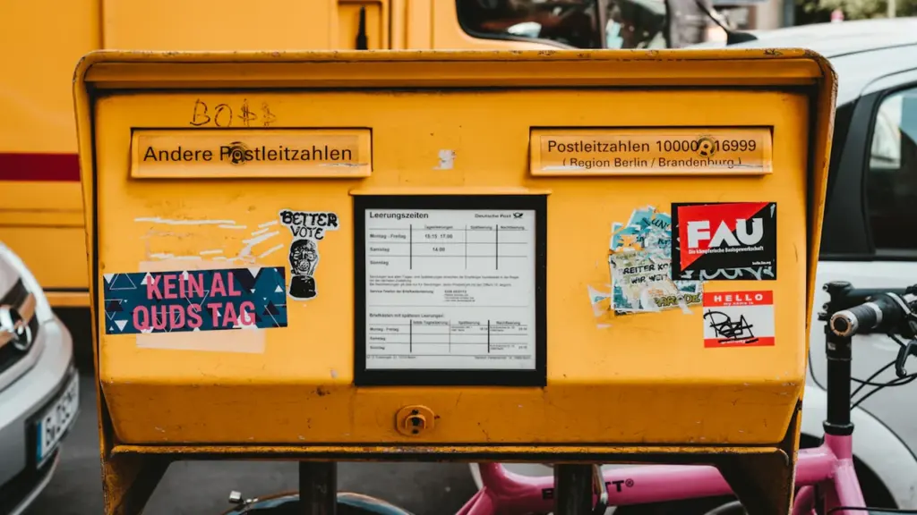 Ein gelber Briefkasten in Berlin mit Aufklebern vor einer belebten städtischen Kulisse.