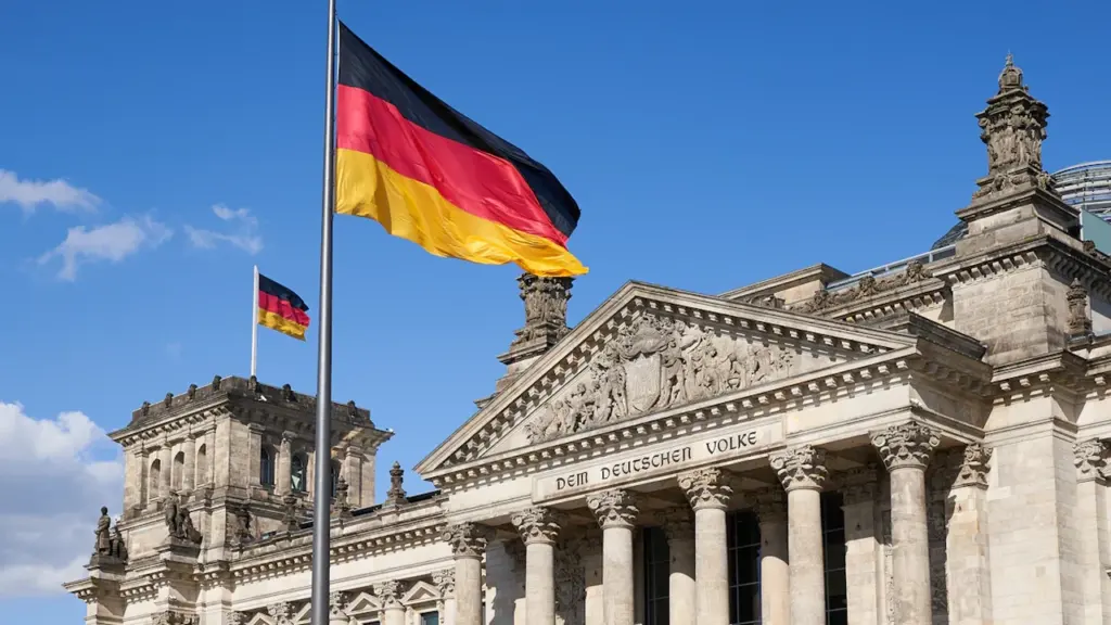 Die deutsche Flagge weht vor dem Berliner Reichstagsgebäude bei blauem Himmel.