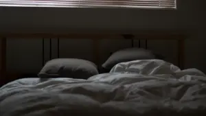 Ein ungemachtes Bett mit heruntergelassenen Jalousien im dunklen Schlafzimmer bei Hitze.