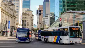Ein Linienbus fährt an einer Baustelle mit weißem Bauzaun in der Stadt vorbei.