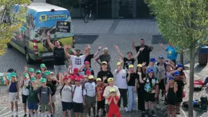 Eine große Gruppe von Kindern und Jugendlichen winkt fröhlich vor einem bunten Edeka-Lieferwagen.