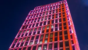 Modernes Hochhaus bei Nacht mit auffälliger pinker und oranger Beleuchtung im Stadtzentrum.
