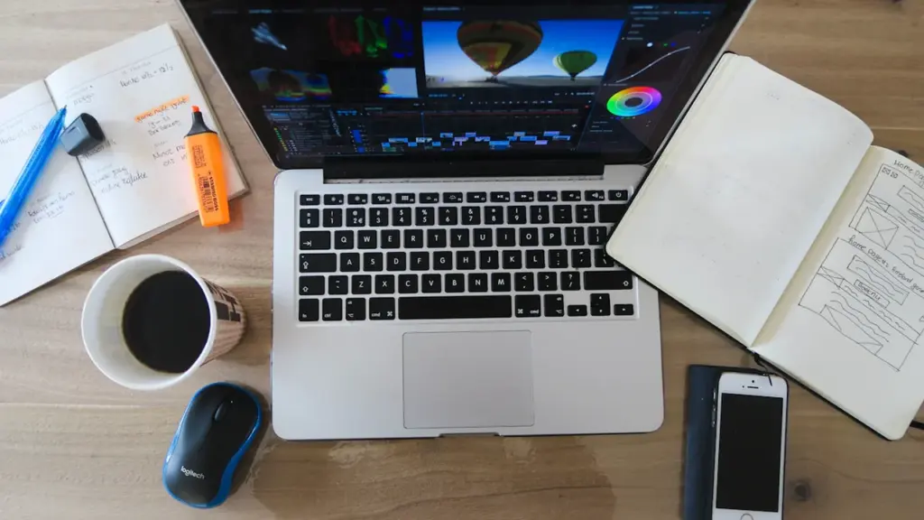 Ein Laptop mit Bildbearbeitungssoftware auf einem Schreibtisch mit Notizbüchern und Kaffee.