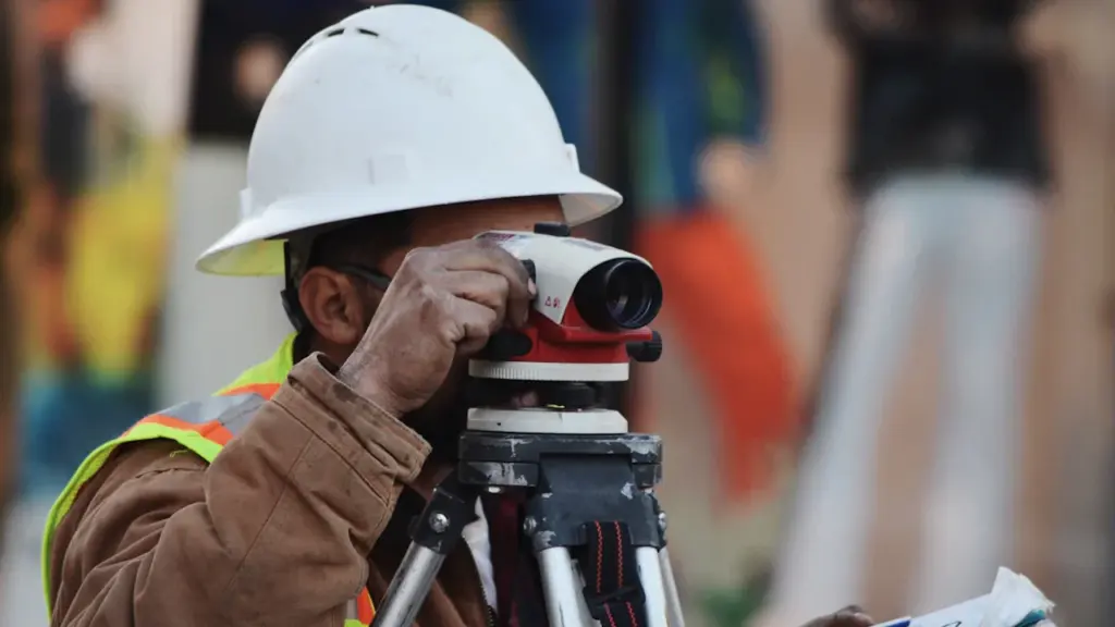 Bauarbeiter mit Schutzhelm bei der Vermessung an einem heißen Sommertag auf der Baustelle.