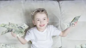 Ein kleines Mädchen sitzt auf einem Sofa und hält zahlreiche US-Dollarnoten in ihren Händen.