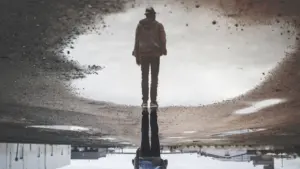 Eine Person steht an einer Pfütze und betrachtet ihr eigenes Spiegelbild.