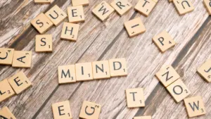 Scrabble-Buchstaben auf einem Holztisch, die das Wort Mind bilden für Achtsamkeit.