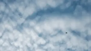 Ein einsames Flugzeug fliegt hoch oben durch einen weiten, bewölkten Himmel.