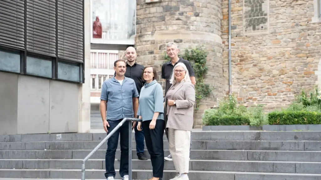 Eine Gruppe von fünf Personen steht auf einer Steintreppe vor einem historischen Steingebäude.