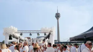 Viele Menschen in weißer Kleidung feiern bei sonnigem Wetter vor dem Düsseldorfer Rheinturm.