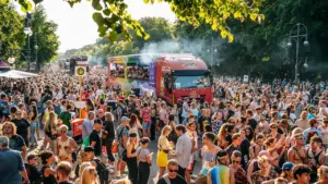 Große Menschenmenge bei einer sommerlichen Outdoor-Veranstaltung mit einem auffälligen roten Lastwagen.