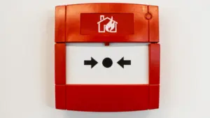 Ein roter Rauchmelder-Druckknopf an einer weißen Wand zur Sicherheit im Haus.
