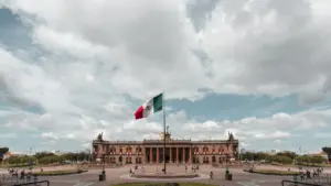 Die mexikanische Flagge weht stolz vor einem historischen Gebäude unter einem bewölkten Himmel.
