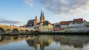 Die historische Steinerne Brücke in Regensburg mit dem Regensburger Dom im Hintergrund bei Tageslicht.