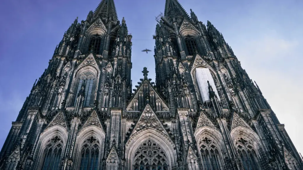 Kölner Dom bei Dämmerung mit Spiegelung im Rhein und beleuchteter Brücke.