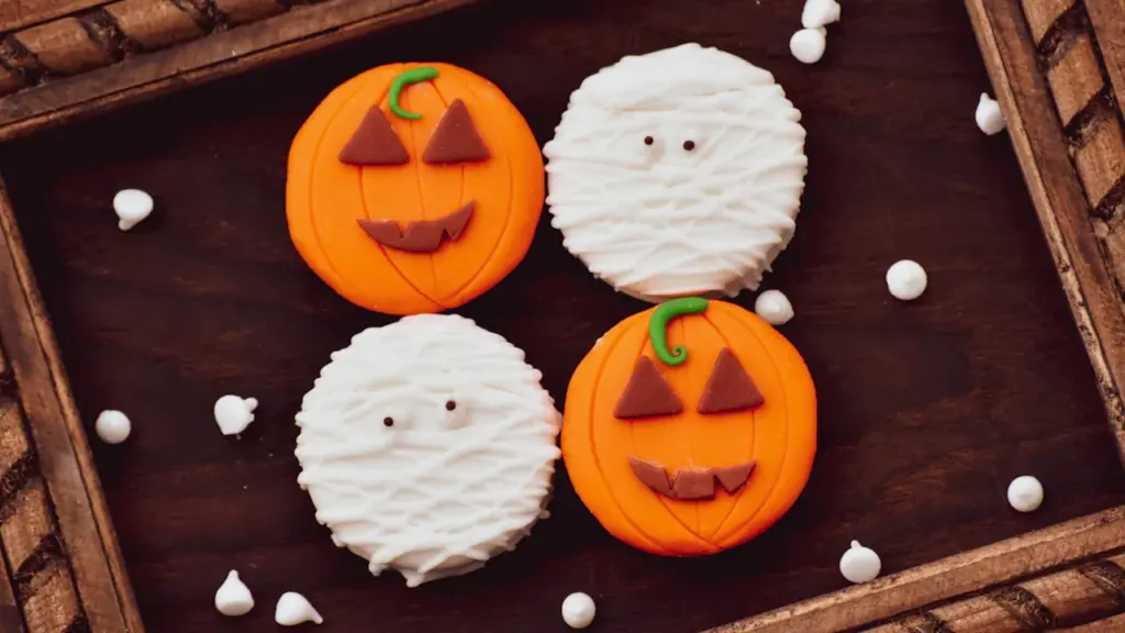 Dekorative Halloween-Kekse in Kürbis- und Mumienform auf einem rustikalen Holzuntergrund arrangiert.