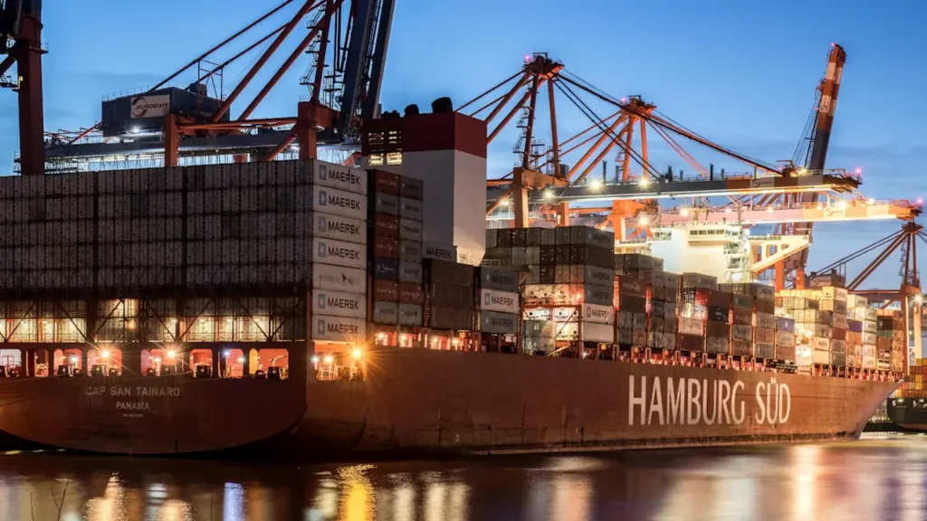 Ein großes Containerschiff liegt abends im belebten Hamburger Hafen vor Anker.