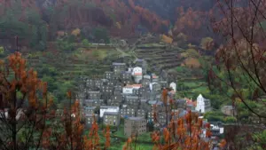 Ein abgelegenes, historisches Steindorf in einer herbstlichen Landschaft mit einer kleinen weißen Kirche.