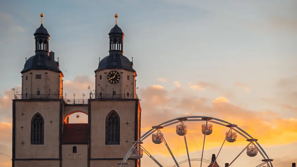 Kirchtürme der Schlosskirche in Lutherstadt Wittenberg vor einem Riesenrad bei goldenem Sonnenuntergang.