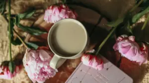 Tasse Kaffee und rosa Pfingstrosen neben einem Tagebuch mit Sternenbildern am Morgen.