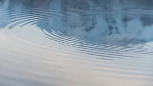 Sanfte konzentrische Wasserwellen auf einer ruhigen, spiegelnden Oberfläche an einem sonnigen Tag.